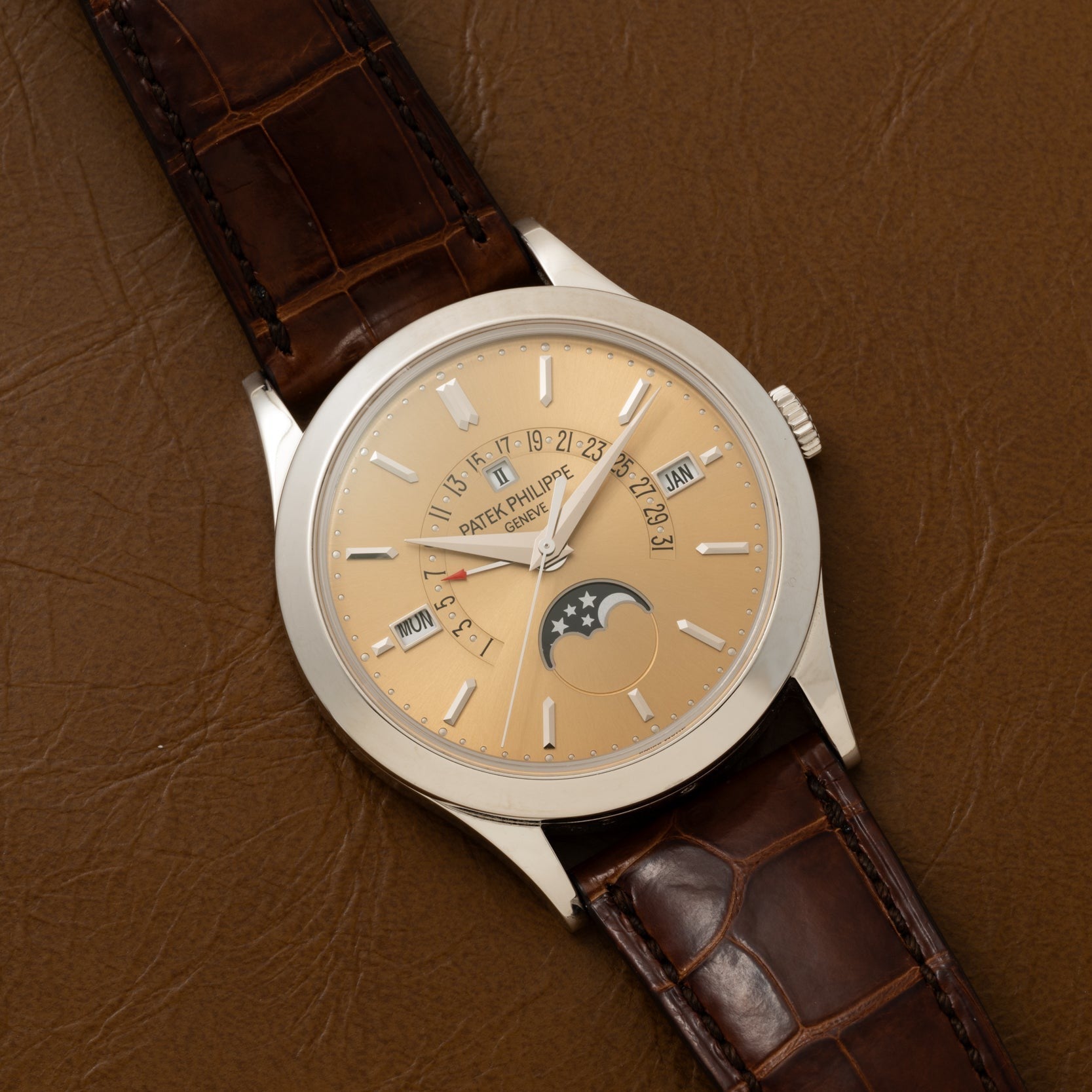 A Patek Philippe Retrograde Perpetual Calendar gold wristwatch with a brown leather strap and moon phase display rests on a brown leather surface.