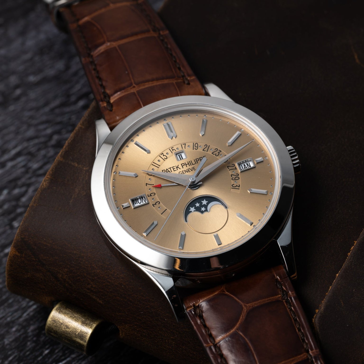 The Patek Philippe Retrograde Perpetual Calendar is a luxury wristwatch with a brown leather strap, gold dial, and features such as moon phase and date display.
