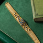 A Patek Philippe Yellow Gold Integrated Dress Watch rests on a green surface beside a green book.