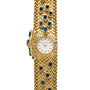 The Patek Philippe Yellow Gold Integrated Dress Watch features a textured gold band and a round white face adorned with blue gemstones.