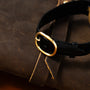Close-up of the Patek Philippe Ellipses black watch strap with a gold buckle, resting on a brown leather surface.