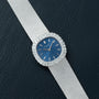 The Patek Philippe Ellipse Ladies Dress Watch features a silver case, blue face, and diamond bezel, elegantly displayed on black textured leather.
