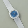The Patek Philippe Ellipse Ladies Dress Watch features a blue face, diamond bezel, and silver strap, displayed on a light gray textured surface.