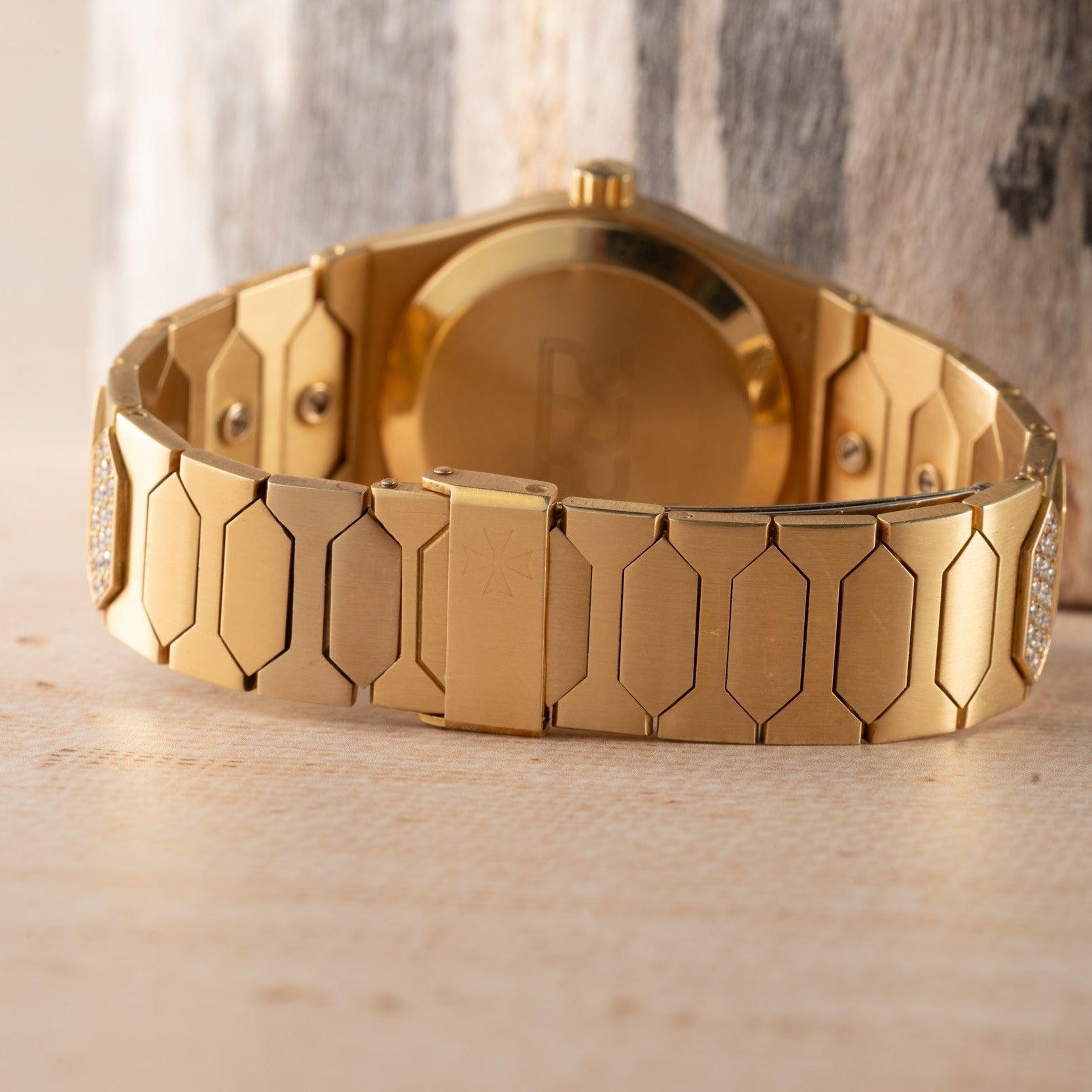 Close-up of the gold metal band and clasp of a Vacheron Constantin 222 luxury wristwatch on a light wooden surface.