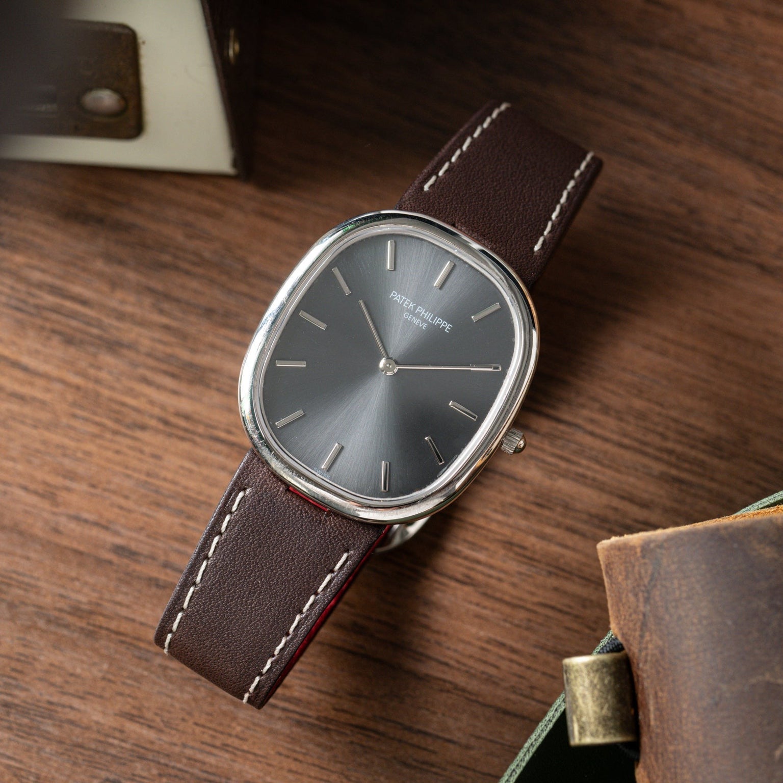 The Patek Philippe Ellipse watch with a brown leather strap rests on a wooden surface.