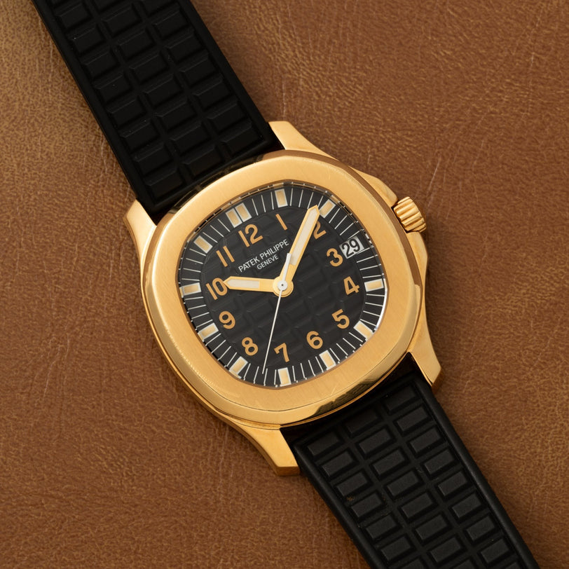 Patek Philippe Aquanaut with a black dial and strap, displayed on a brown leather surface.