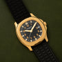 The Patek Philippe Aquanaut wristwatch with a black strap is displayed on a green surface, showing the time as 12:15 and the date as 29.