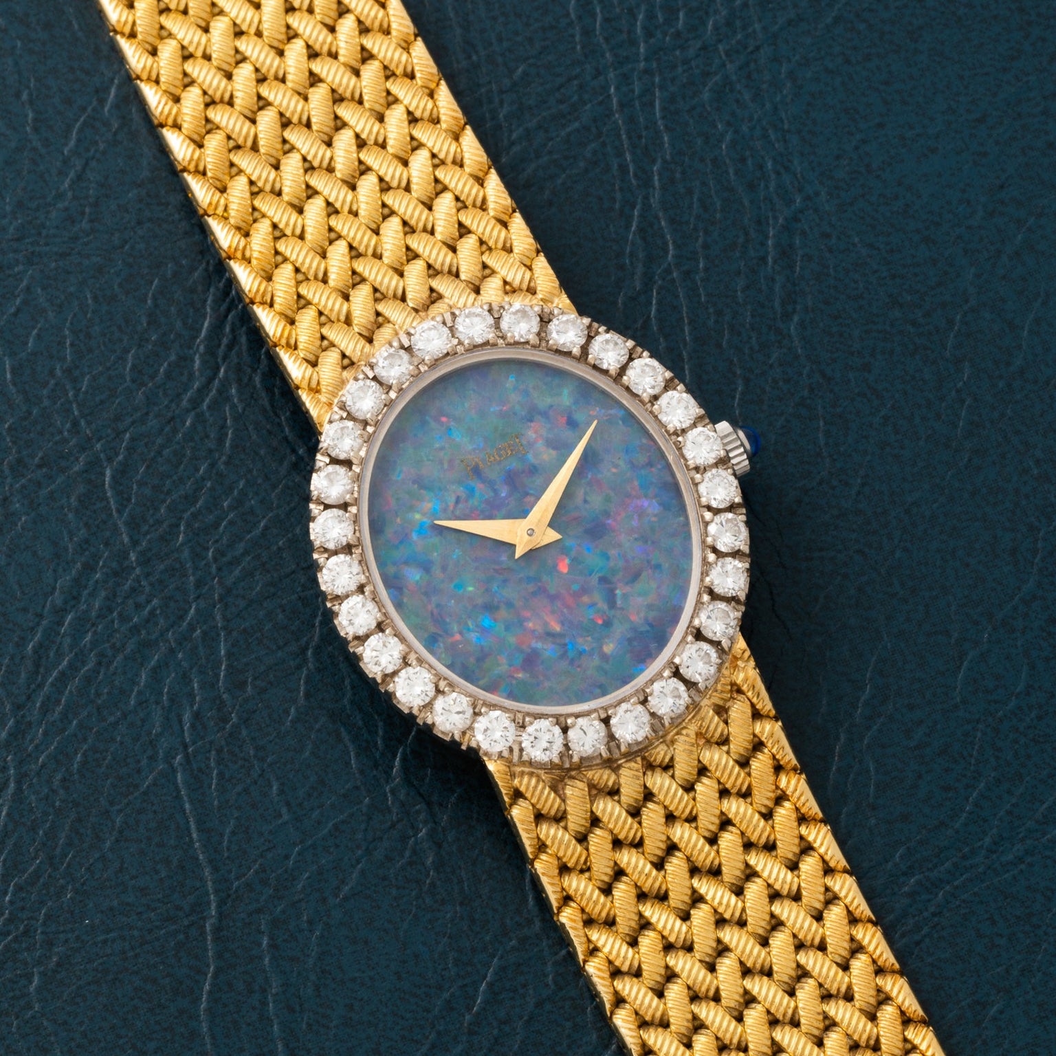 The Piaget Opal Yellow Gold Dress Watch features a jeweled bezel and opal face, elegantly displayed on a dark textured surface.