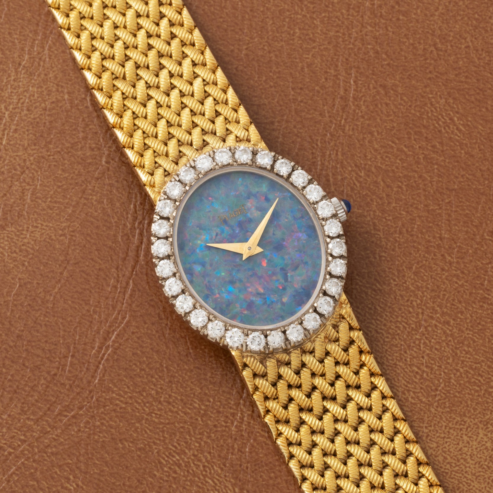 Piaget Opal Yellow Gold Dress Watch with a textured band, opal face, and diamond bezel displayed on a brown leather surface.