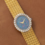 Piaget Opal Yellow Gold Dress Watch with a textured band, opal face, and diamond bezel displayed on a brown leather surface.