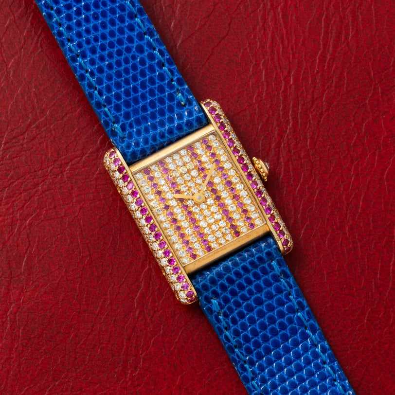 The Cartier Tank Louis Diamonds features a bejeweled face with diamonds and pink gemstones, a blue strap on red leather, and a gold case.