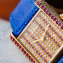 Close-up of the Cartier Tank Louis Diamonds watch featuring a blue strap, gold case, and a diamond and ruby-encrusted face.