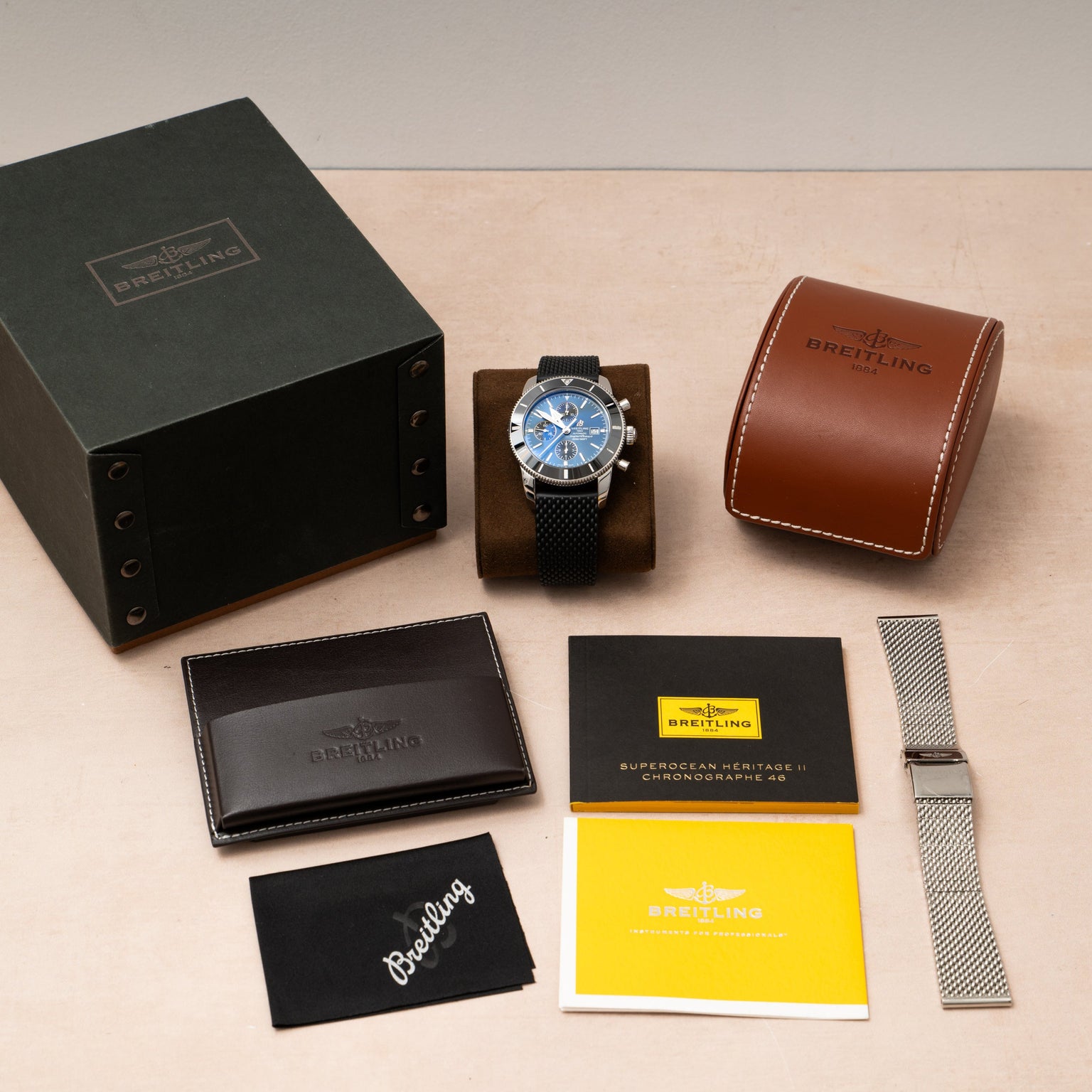 A Breitling SuperOcean B01 Chronograph 44 watch, complete with box, case, extra strap, and documents, is arranged neatly on a light surface.