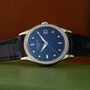The Patek Philippe Calatrava Diamond Bezel, featuring a blue face, diamond markers, and a black leather strap, rests on a green surface.
