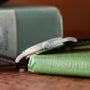 A close-up side view of the Patek Philippe Calatrava Diamond Bezel wristwatch in silver, resting on a green hardcover book.