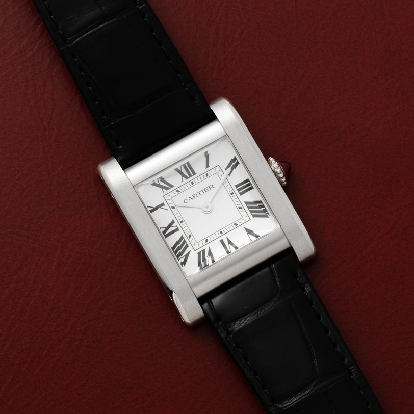 The Cartier Tank Normale features a rectangular face, Roman numerals, and a black leather strap set against red leather.