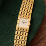 A Piaget Dancer gold watch with a diamond-studded face rests on a green textured surface.