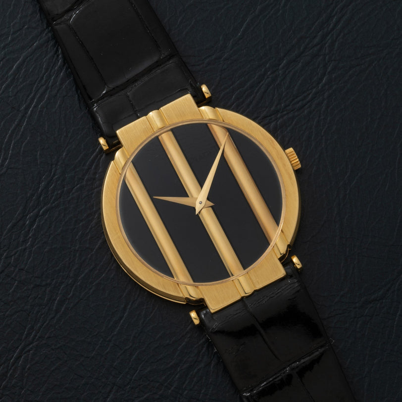 The Piaget Polo Onyx gold watch features a black face, three vertical gold bars, and a black leather strap, displayed on a textured black surface.