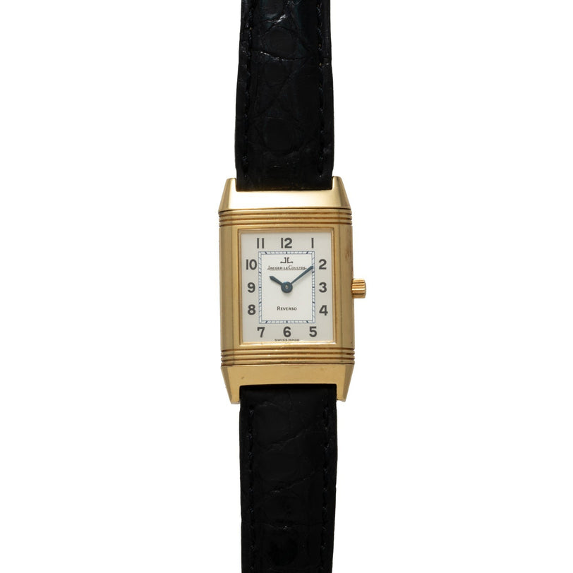 The Jaeger-LeCoultre Reverso Classique is a gold rectangular wristwatch by Jaeger-LeCoultre, featuring a white dial with Arabic numerals and a black leather strap.