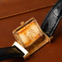 A Jaeger-LeCoultre Reverso Classique gold wristwatch with a worn, engraved back reading M J rests on brown leather.