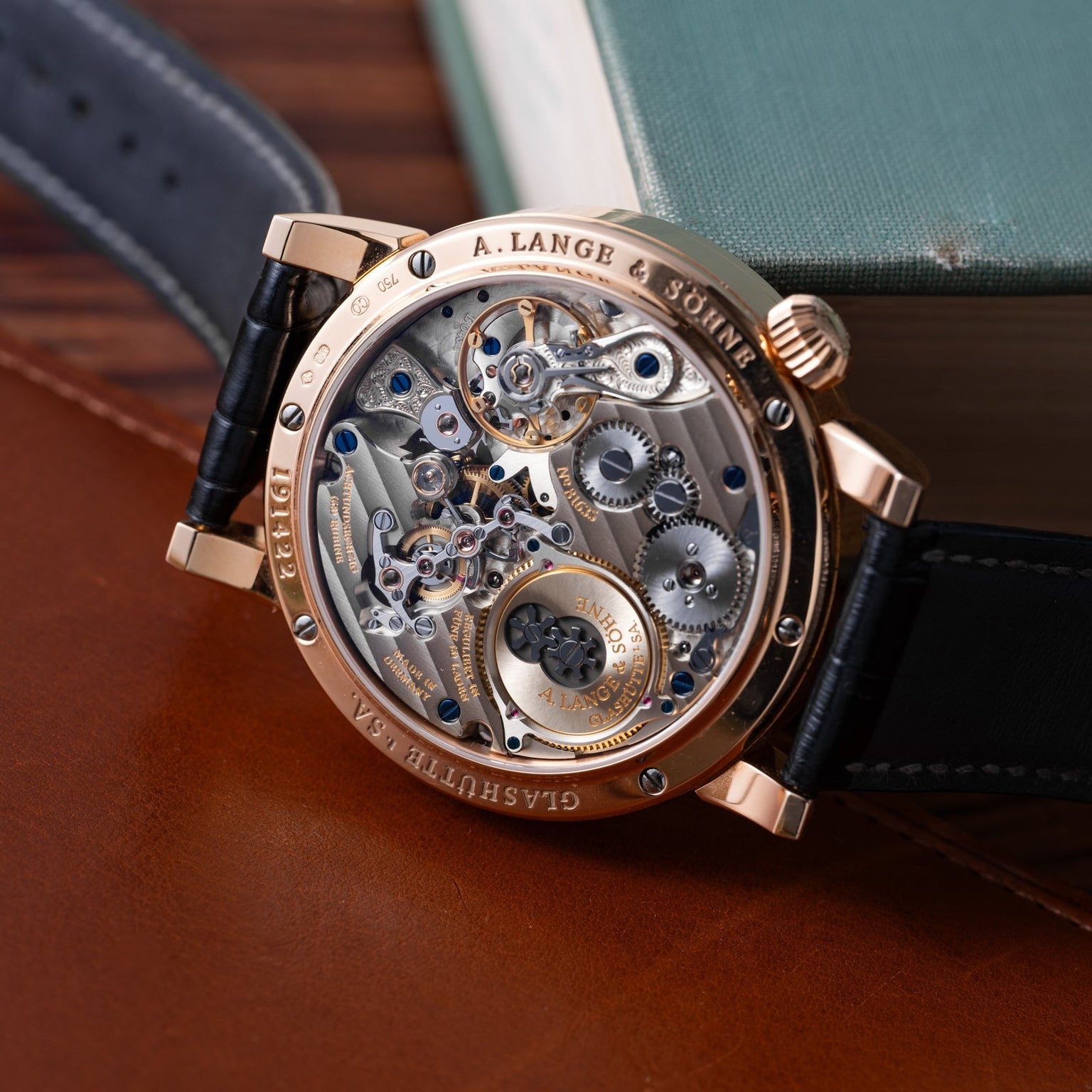 The Lange & Sohne Zeitwerk, featuring an exposed mechanical movement, is displayed on a brown leather surface.