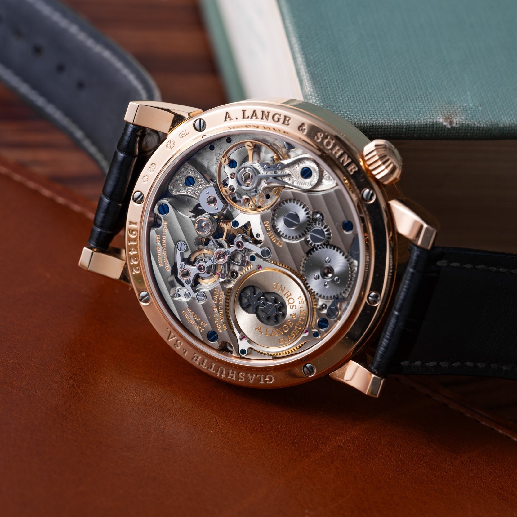 The Lange & Sohne Zeitwerk, featuring an exposed mechanical movement, is displayed on a brown leather surface.