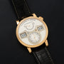 The Lange & Sohne Zeitwerk watch features a digital time display and black leather strap, shown on a black surface.
