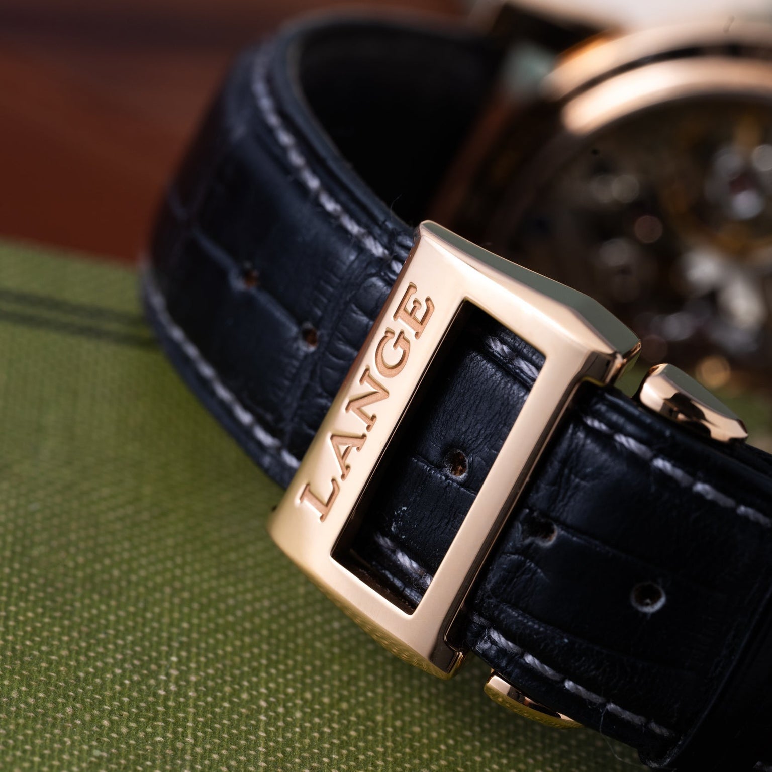 Close-up of the Zeitwerks black leather strap with a gold clasp engraved with Lange & Sohne, resting on green fabric.