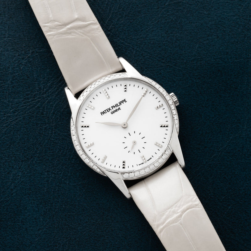 A Patek Philippe Calatrava wristwatch with a diamond bezel rests on a dark textured surface.