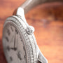 Close-up of a Patek Philippe Calatrava luxury silver wristwatch featuring a diamond-set bezel and crown, displayed on a wooden surface.
