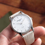 A hand holding a Patek Philippe Calatrava wristwatch with a diamond bezel and leather strap.