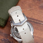 Close-up of the Patek Philippe Calatravas white leather strap with a silver buckle, displayed on a wooden surface.