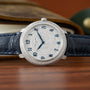 A Patek Philippe Calatrava watch with diamonds and a black leather strap displayed on a wooden surface.