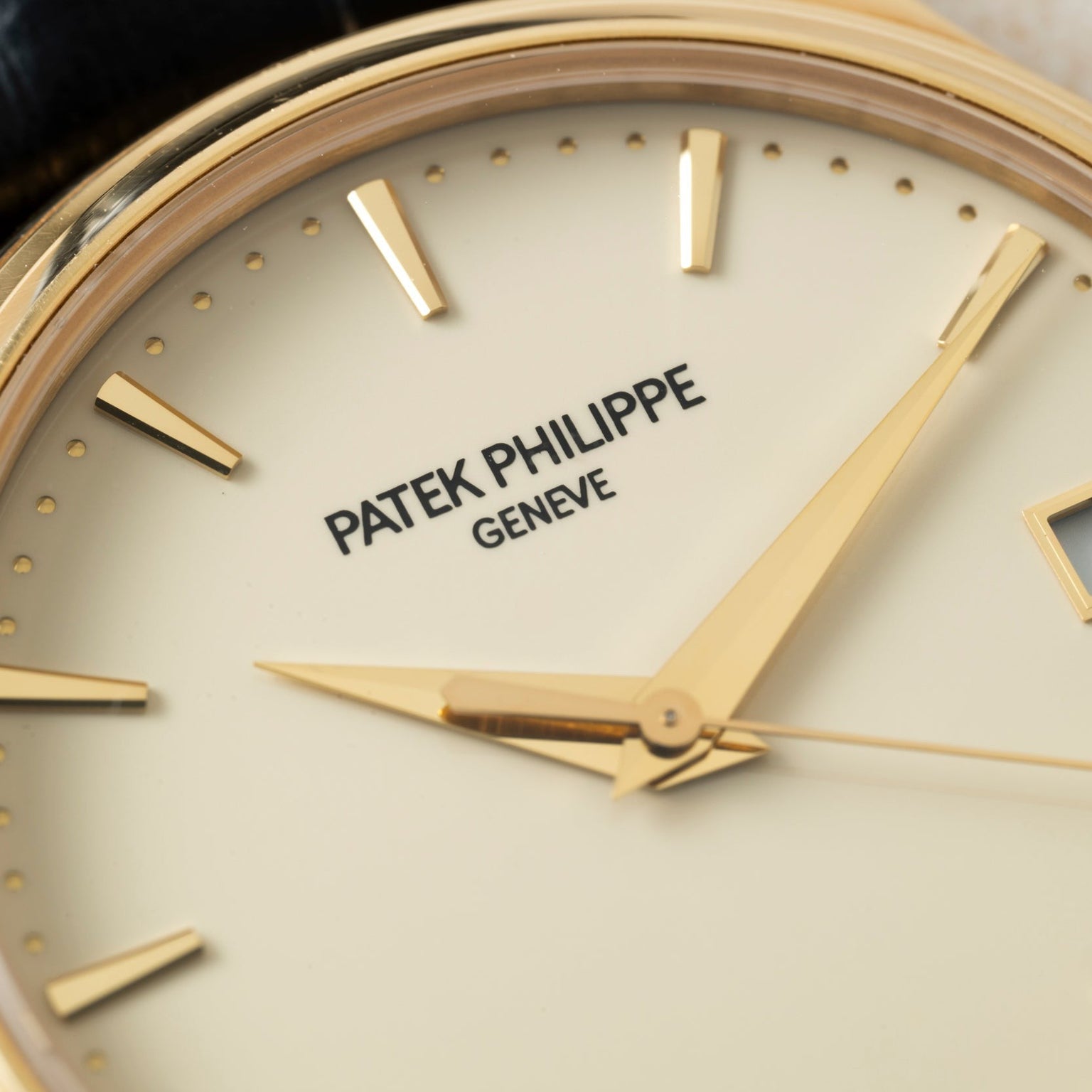 Close-up of a Patek Philippe Calatrava watch face with gold hands and hour markers.