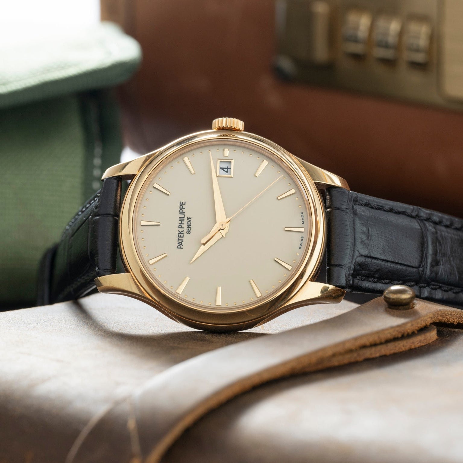 The Patek Philippe Calatrava, featuring a gold case, black leather strap, and white dial, rests on a leather surface.