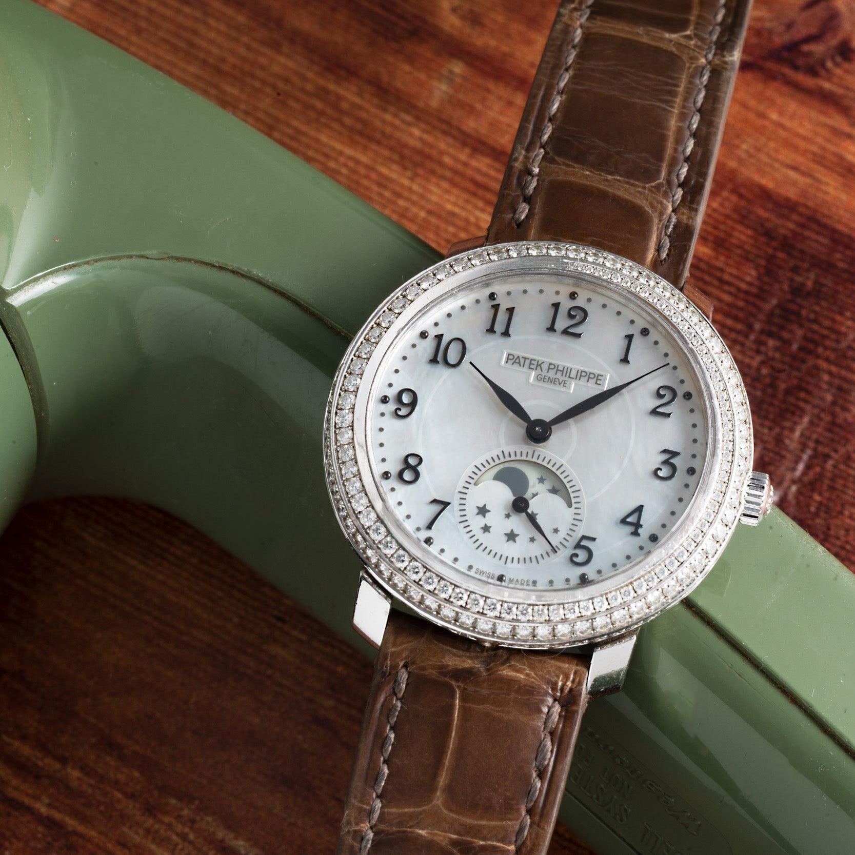 A Patek Philippe Ladies Complication watch with a brown leather strap is displayed on a vintage green telephone.