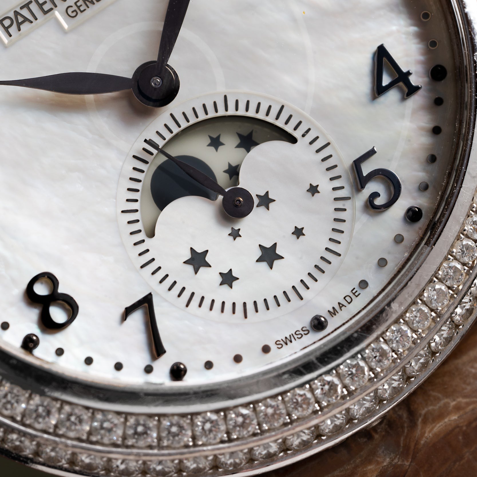 Close-up of the Patek Philippe Ladies Complication watch face, featuring a moon phase display, star details, diamond bezel, and visible numbers 4, 5, 7, and 8.