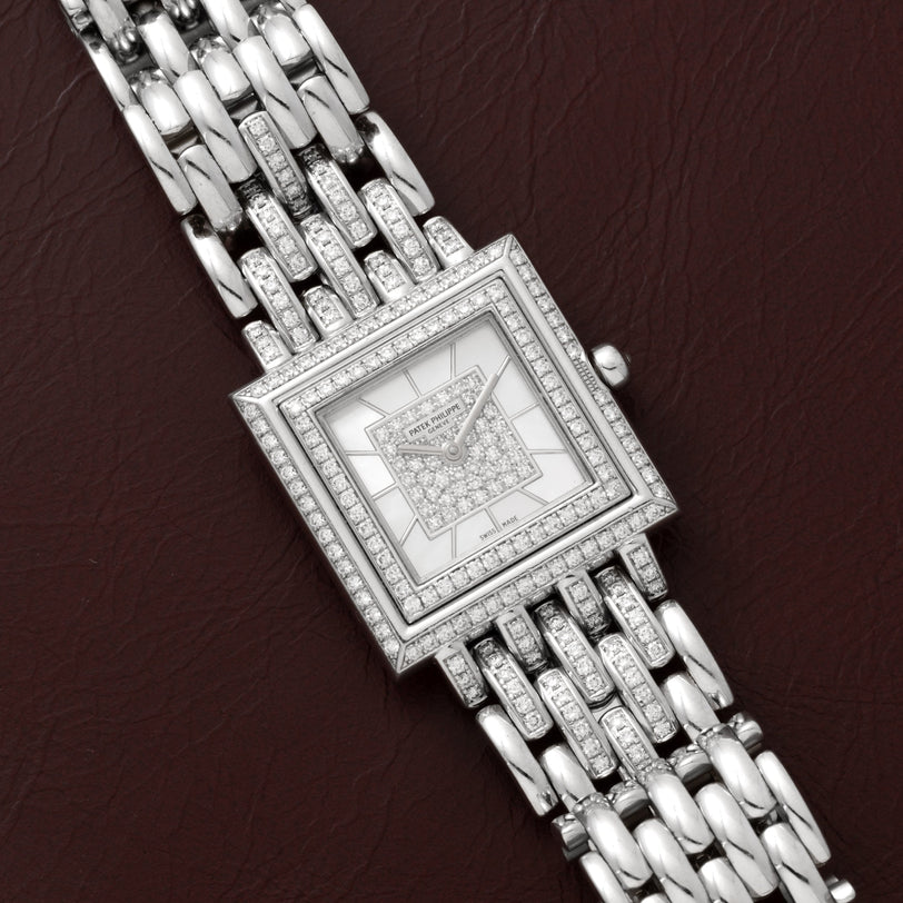 Patek Philippe Gondolo square silver wristwatch with diamond accents displayed on a brown leather surface.