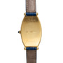 Cartier Tonneau XL watch with gold case, blue leather strap, engraved details, and a gemstone crown on the left side.