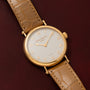 The Patek Philippe Calatrava wristwatch with a tan leather strap rests on a dark brown textured surface.
