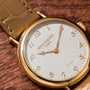 Patek Philippe Calatrava gold wristwatch with a brown leather strap displayed on a textured brown surface.
