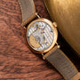 The Patek Philippe Calatrava gold wristwatch, featuring a visible intricate mechanical movement, is displayed on a wooden surface next to a brass object.