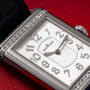 A close-up of the Jaeger-LeCoultre Reverso Classique Ladies watch, a luxury rectangular timepiece with diamond accents by Jaeger-LeCoultre, displayed on a red textured surface.