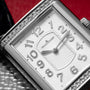 Close-up of the Jaeger-LeCoultre Reverso Classique Ladies watch, featuring a luxury rectangular design with diamond bezel and silver numerals on a textured white dial.