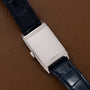 The Jaeger-LeCoultre Reverso Classique Ladies features a silver rectangular case, minimalist dial, and a blue leather strap, displayed on a brown leather surface.