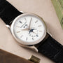 The Patek Philippe Annual Calendar Moonphase is a luxury wristwatch featuring a white dial, black leather strap, and displays for day, date, and moon phase.