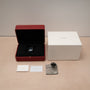 A Cartier Privé Collection Tank Asymétrique New York Edition watch in a red box, with a white outer box, cards, cloth, and magnifier displayed on a beige surface.