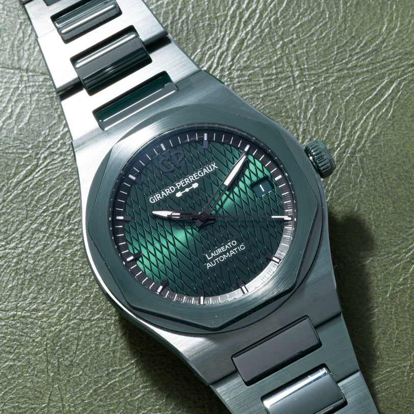 The Girard-Perregaux Laureato Green Ceramic Aston Martin Edition features a green textured dial, showcased on a green leather surface.