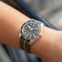 A TUDOR Black Bay 58 Silver wristwatch with a fabric strap is worn on a person’s wrist.