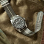 The TUDOR Black Bay 58 Silver wristwatch with a gray fabric strap rests on an olive green canvas surface.
